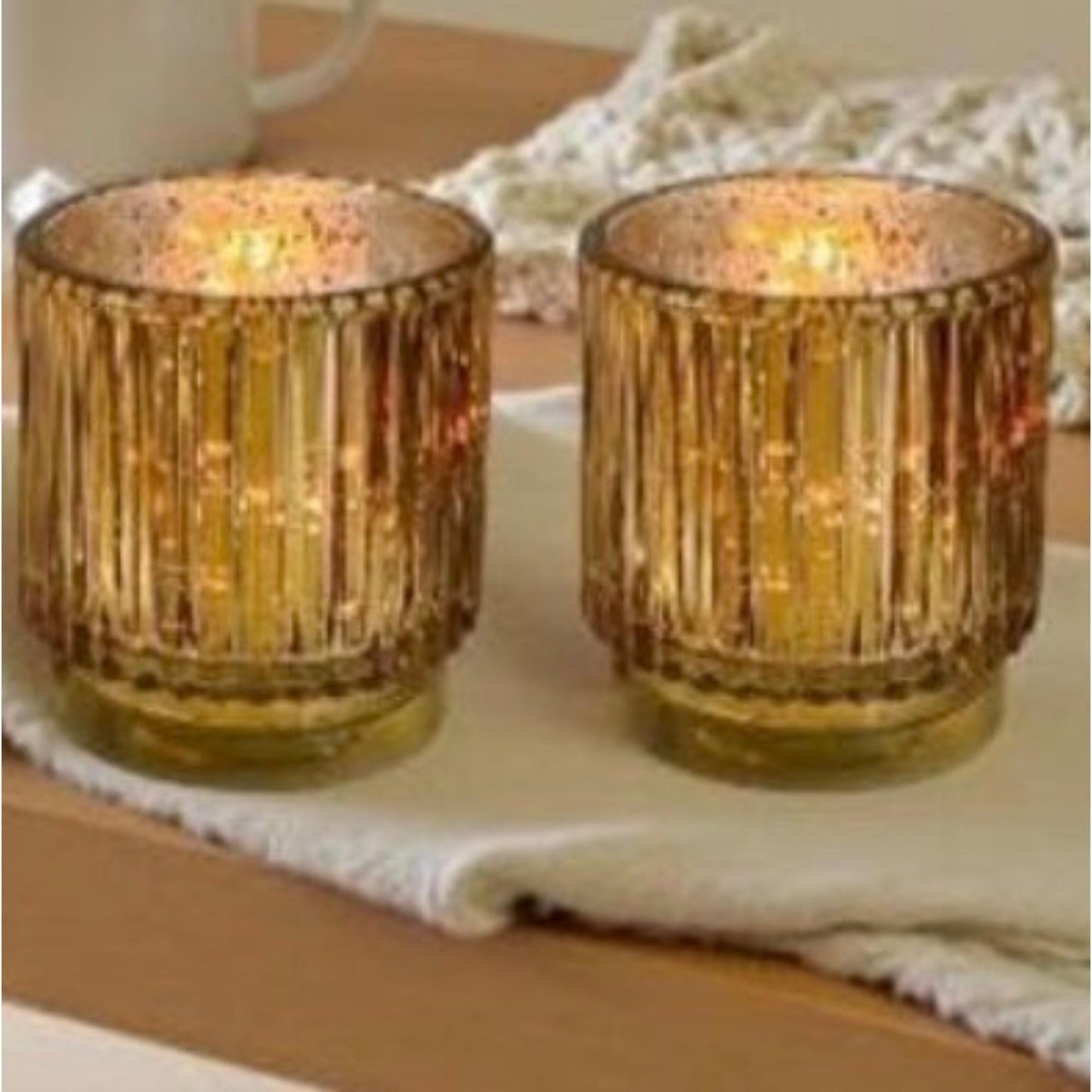 Two gold candle holders with a soft glow on a white surface.