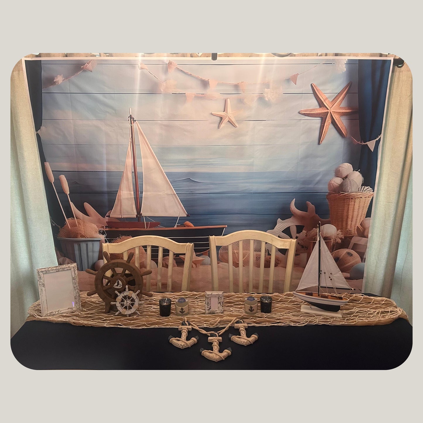 Decorative scene with sailboats, anchors and a ship wheels on a navy blue surface with a scenic background.