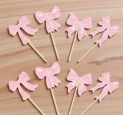Pink bows on sticks arranged on a wooden surface as cupcake toppers