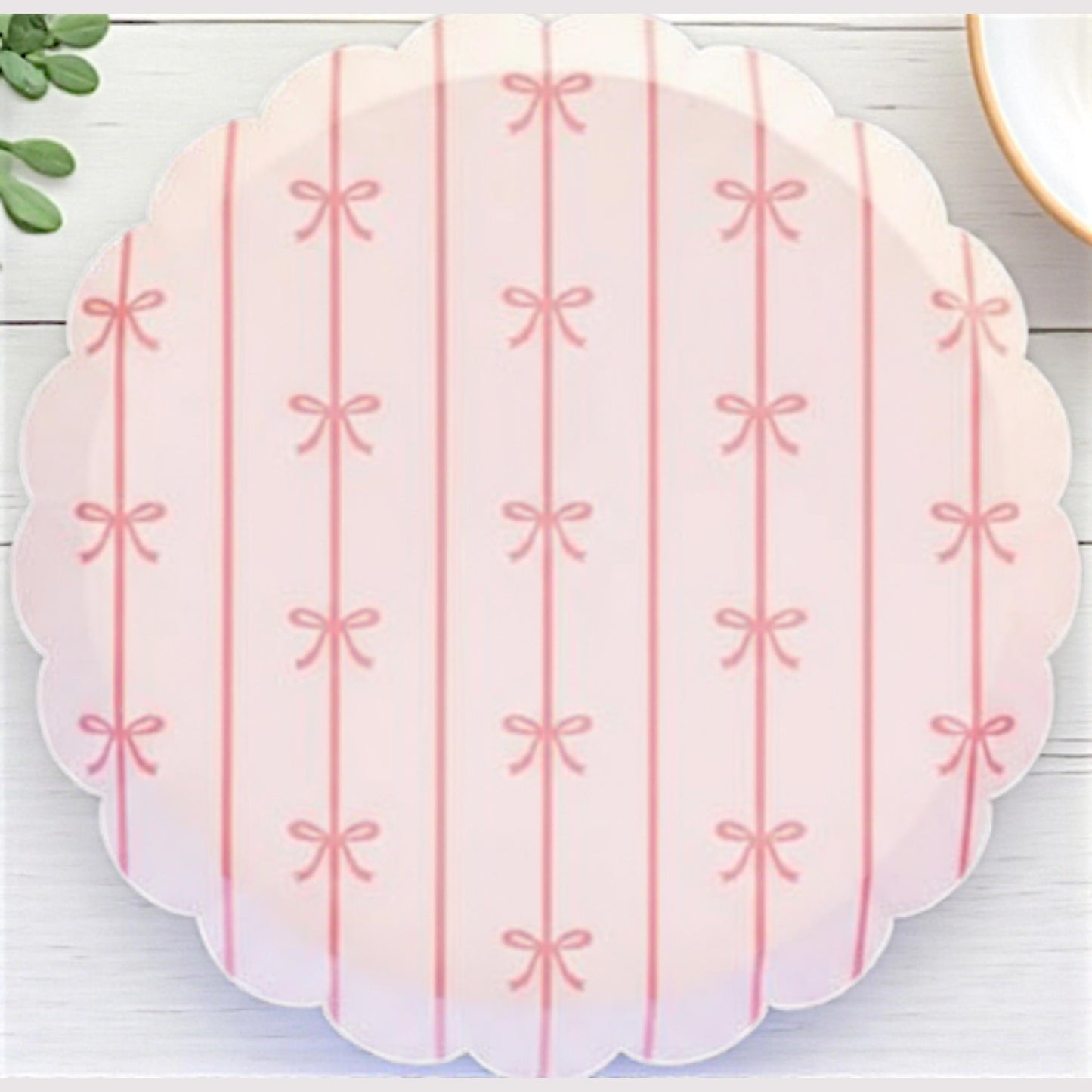 Scalloped pink bow party dessert plate with bow pattern on a white wooden surface