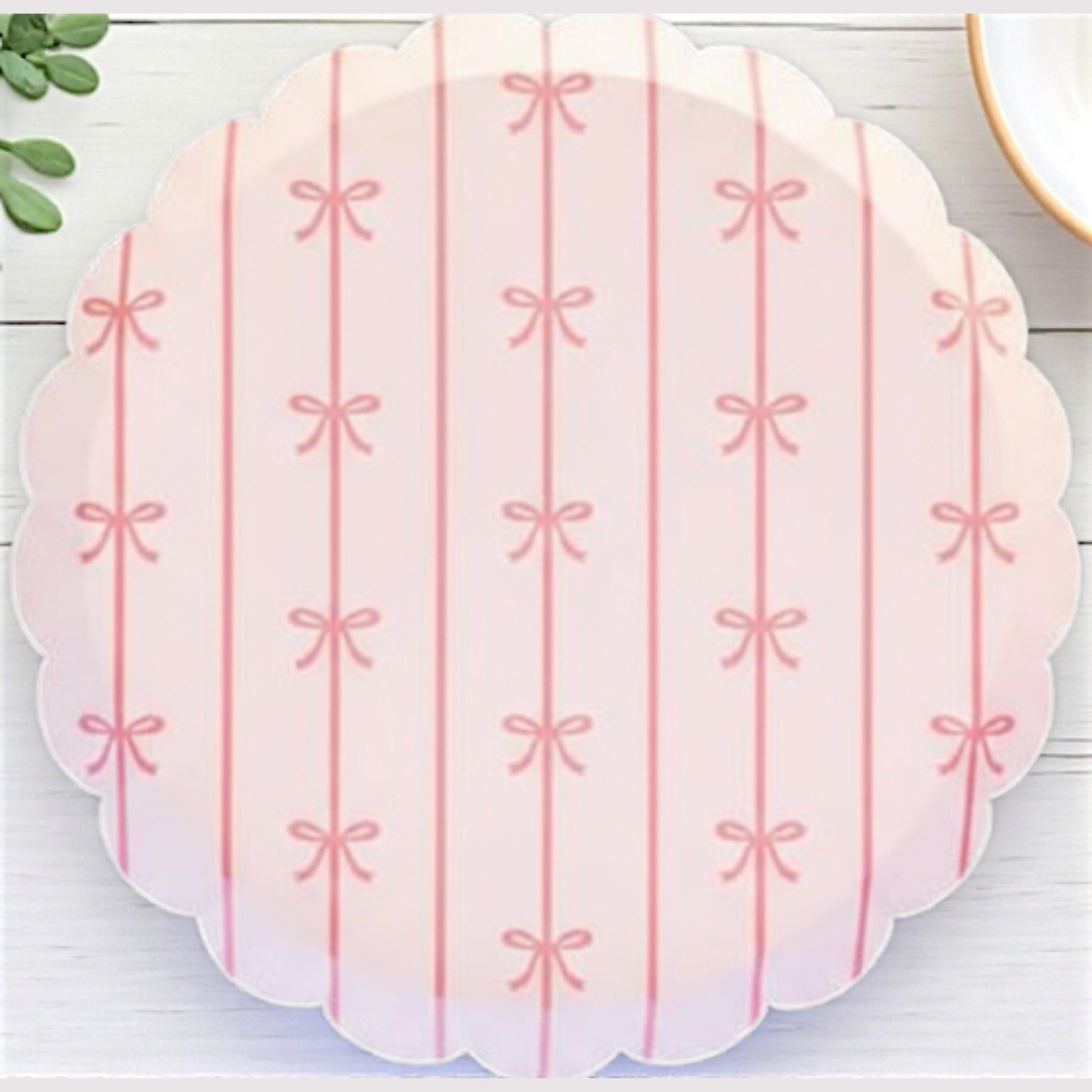 Scalloped pink bow party dessert plate with bow pattern on a white wooden surface