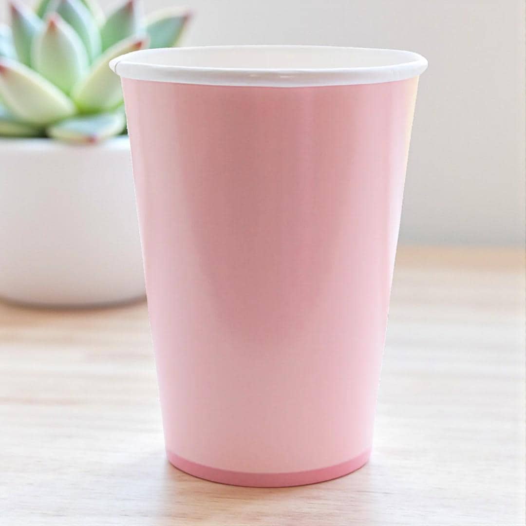 Pink paper cup on a light wooden surface with a blurred plant in the background